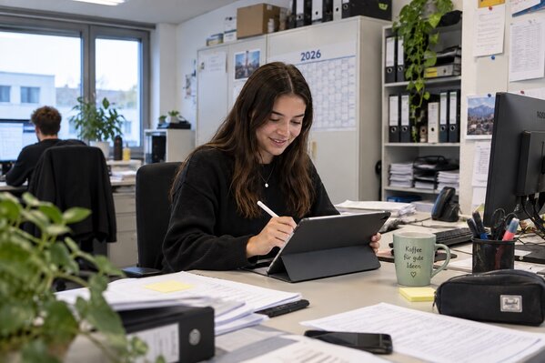Ein Lehrling zur Bürokauffrau sitzt in einem Büro und arbeitet mit einem Tablet 